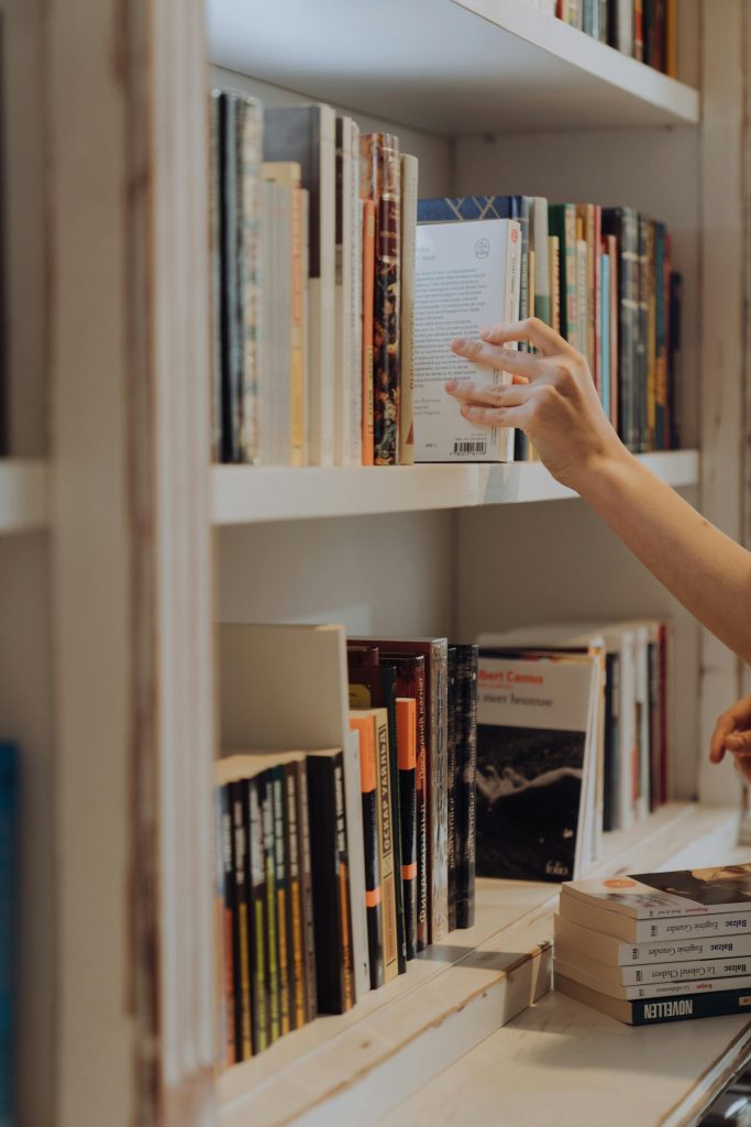 A person organizing books on a library bookshelf, focusing on literature and education.