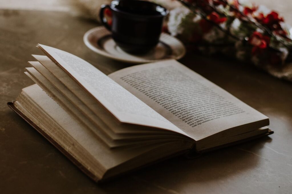 An open book lies on a table beside a coffee cup and flowers, offering a cozy reading ambiance.