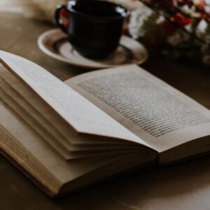 An open book lies on a table beside a coffee cup and flowers, offering a cozy reading ambiance.